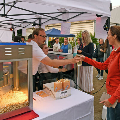 Kellner übergibt ein Getränk am Popcornstand beim Open-Air-Kino im Sportpark Groß-Gerau.