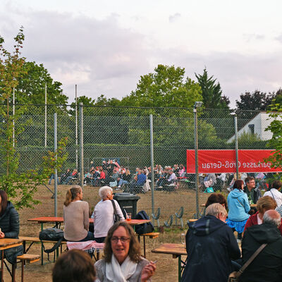 Gäste an Biertischgarnituren beim Open-Air-Kino im Sportpark Groß-Gerau.
