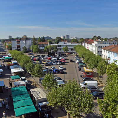 Blick aus der Vogelperspektive auf den Wochenmarkt mit seinen vielfältigen Ausstellern und den Marktplatz-Parkplatz.