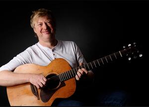 Pressefoto von Paddy Schmidt mit Gitarre in der Hand.