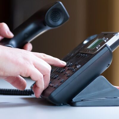 In der einen Hand wird der Telefonh&ouml;rer gehalten und die andere Hand w&auml;hlt eine Nummer.