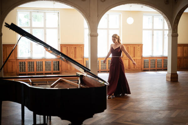 Links im Vordergrund steht ein ge&ouml;ffneter Fl&uuml;gel. Versetzt hintendran ist  die Pianistin Julia Rinderle zu sehen.