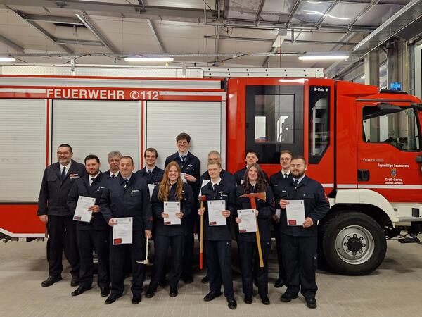 13 ehrenamtliche Feuerwehrleute stehen zusammen vor einem Feuerwehrauto im Ger&auml;tehaus Berkach und erhalten ihre Urkunde zur Bef&ouml;rderung.