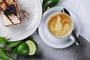 Ein St&uuml;ck Kuchen und eine Tasse Kaffee. Zur Deko liegt noch ein bisschen Minze und eine Limette nebendran.