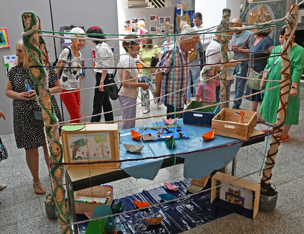 Besucherinnen und Besucher, die ein kreatives Ausstellungsst&uuml;ck mit gespannten Seilen und selbstgestalteten Kisten im Rahmen der Ausstellung "GG - mein Lebensraum" begutachten.