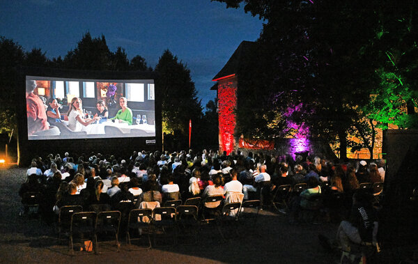 Sitzende Menschen mit Blick auf die gro&szlig;e Open-Air-Kinoleinwand im Schlosshof Dornberg.