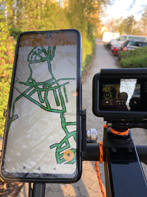 Unter Einsatz eines E-Scooters, der mit hochauflösenden Kameras ausgestattet ist, erfasst ein Straßenbauingenieur den Zustand von Fuß- und Radwegen. Im Bildschirm wird das bereits befahrene Verkehrswegsnetz angezeigt.